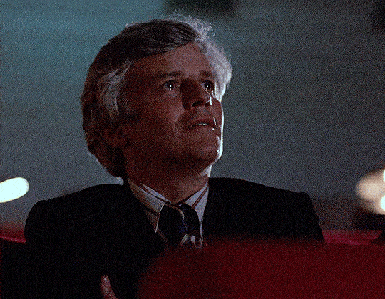A teary eyed man getting overwhelmed by watching screen at theater